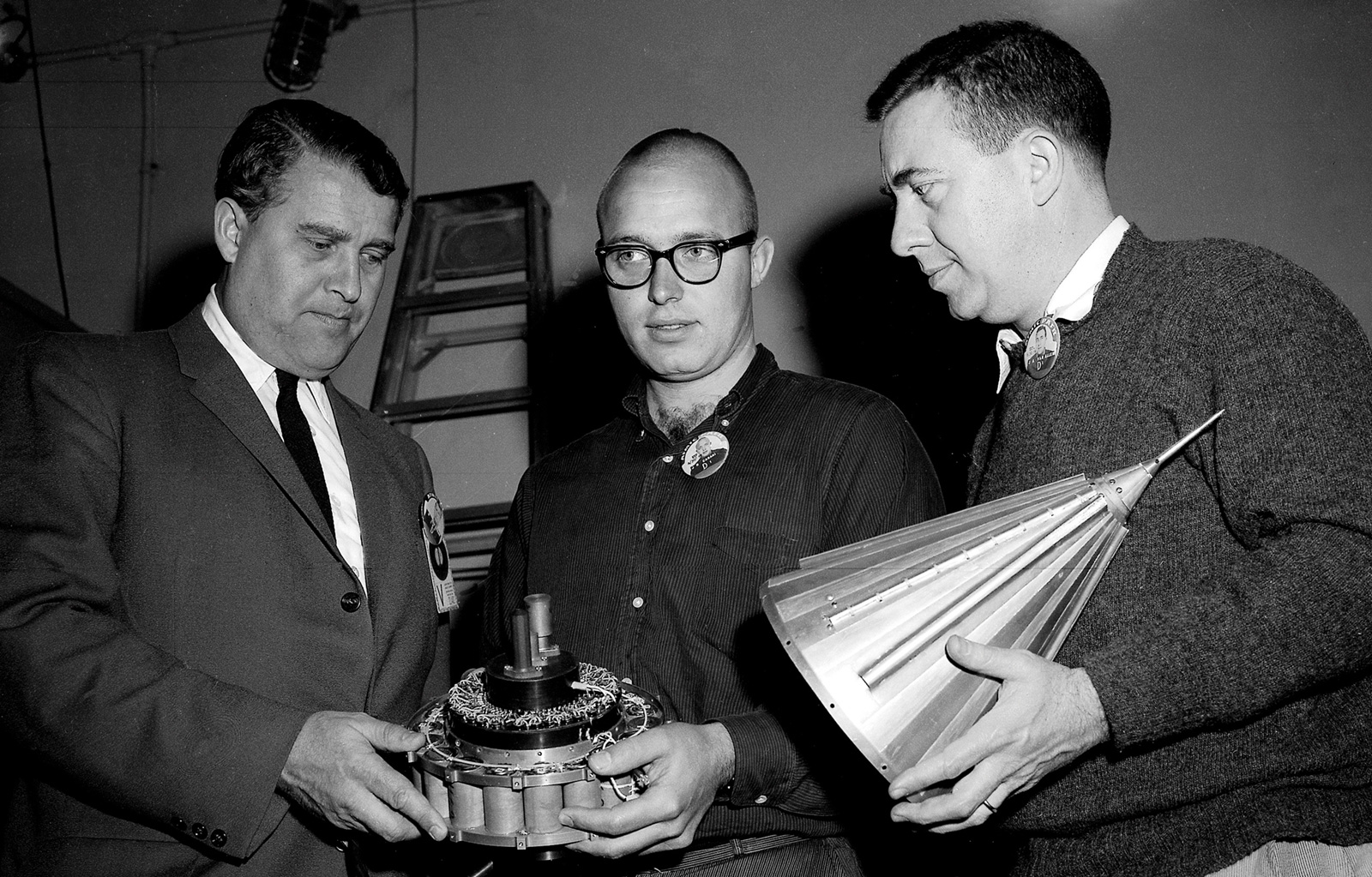 Black and white image of three men holding a small spacecraft.