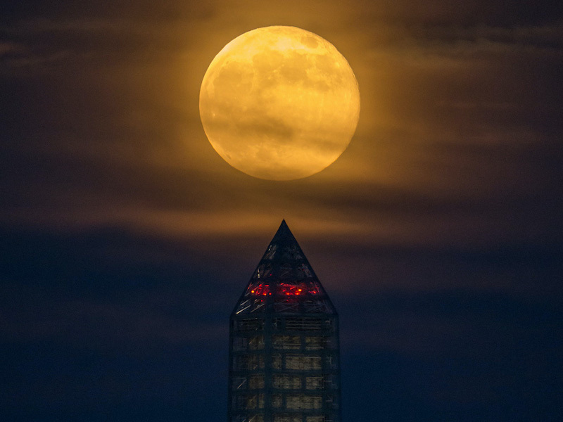 Moon seen through hazy clouds above an obelisk.