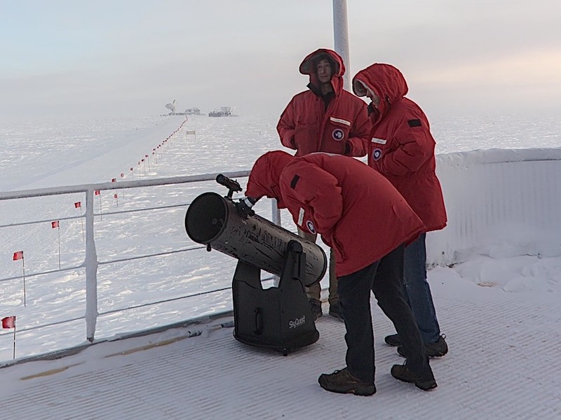 Researchers in red parkas using a telescope at the South Pole