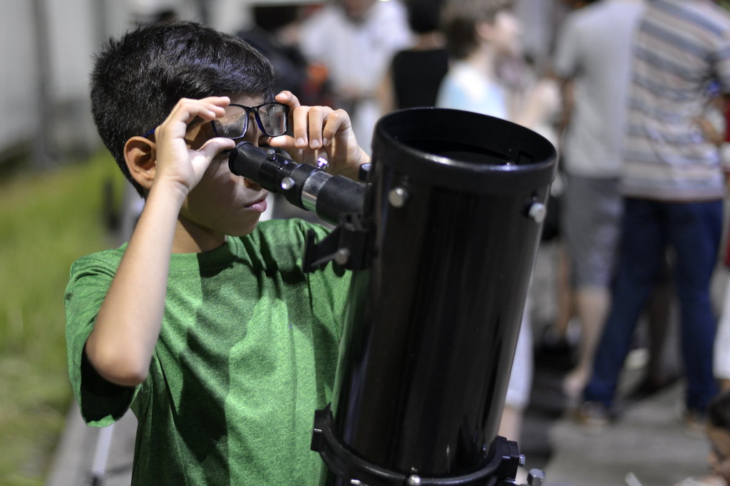 Child lifting eyeglasses to look through a telescope.