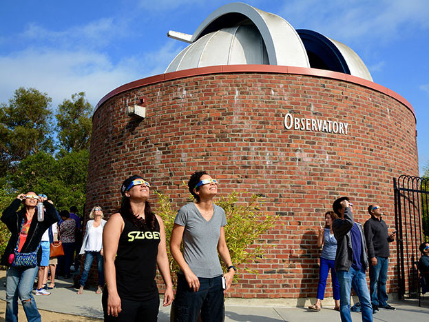 Photo of people walking in with brick buildling housing a large telescope