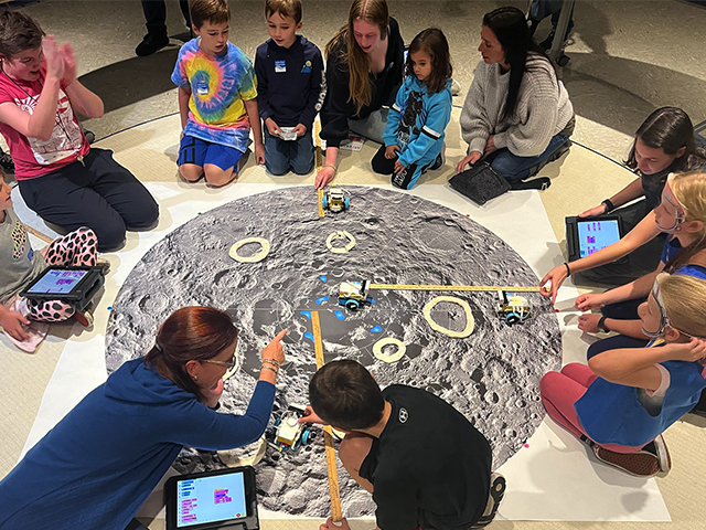 Group of people sitting on the floor surrounding a large poster of the Moon.