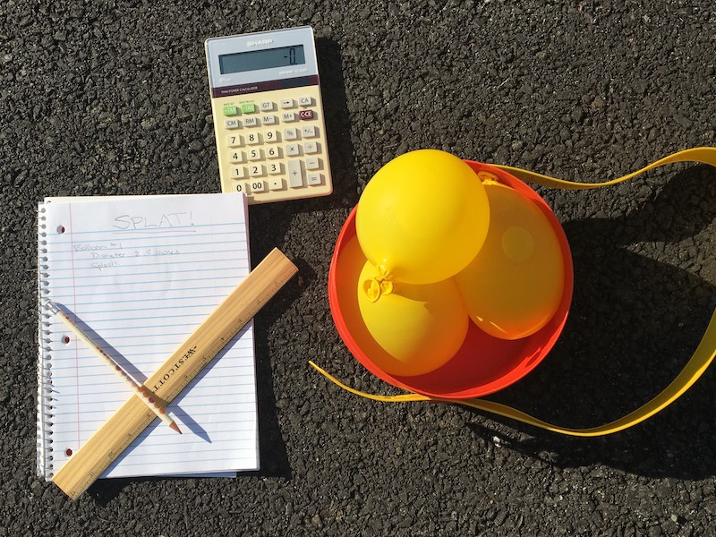 Water balloon, calculator, and notebook on pavement.