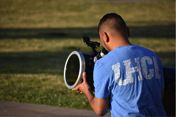 Photo of a person with his back to the camera looking into a telescope.