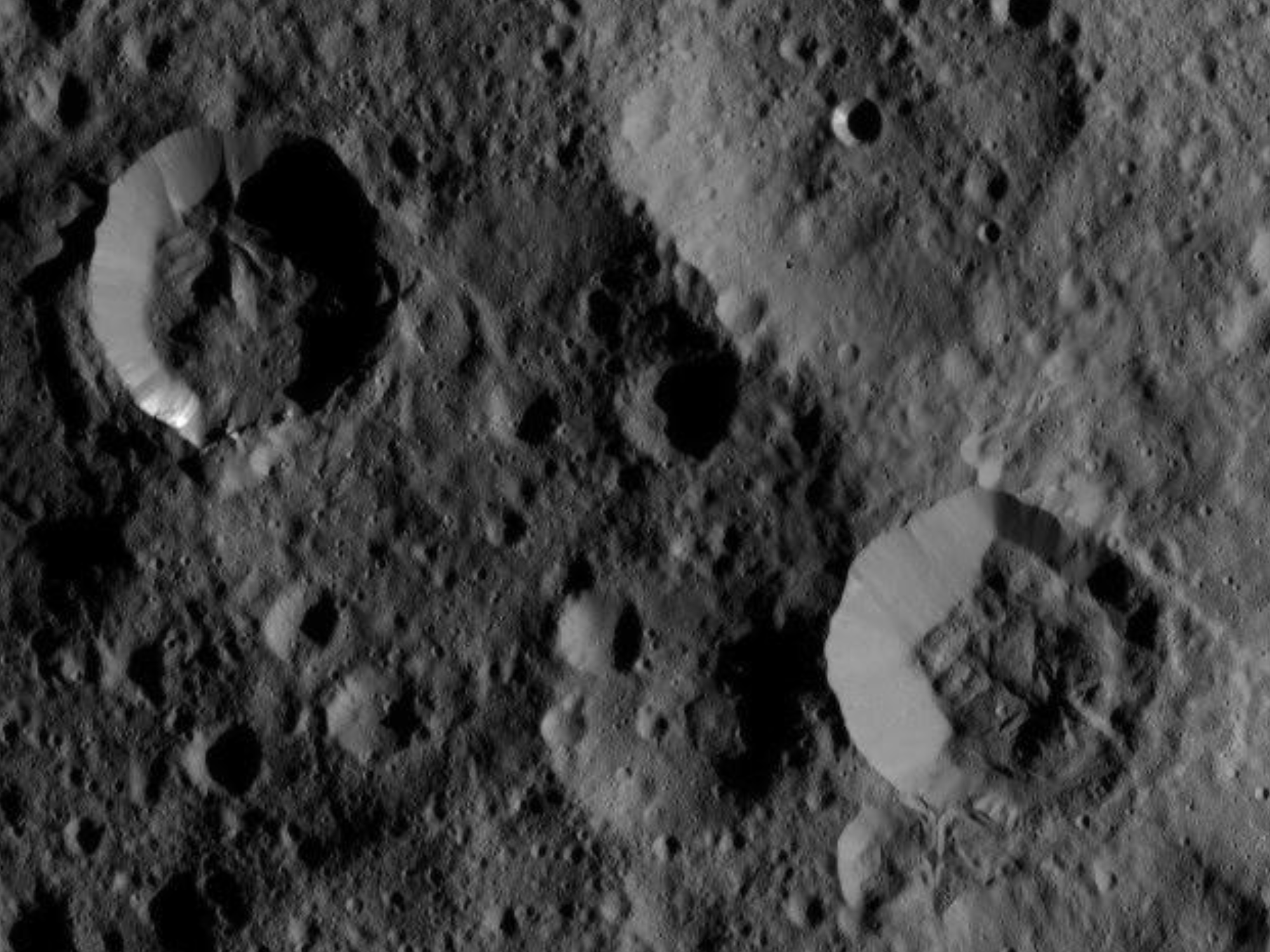 Overhead view of craters in grey lunar terrain.