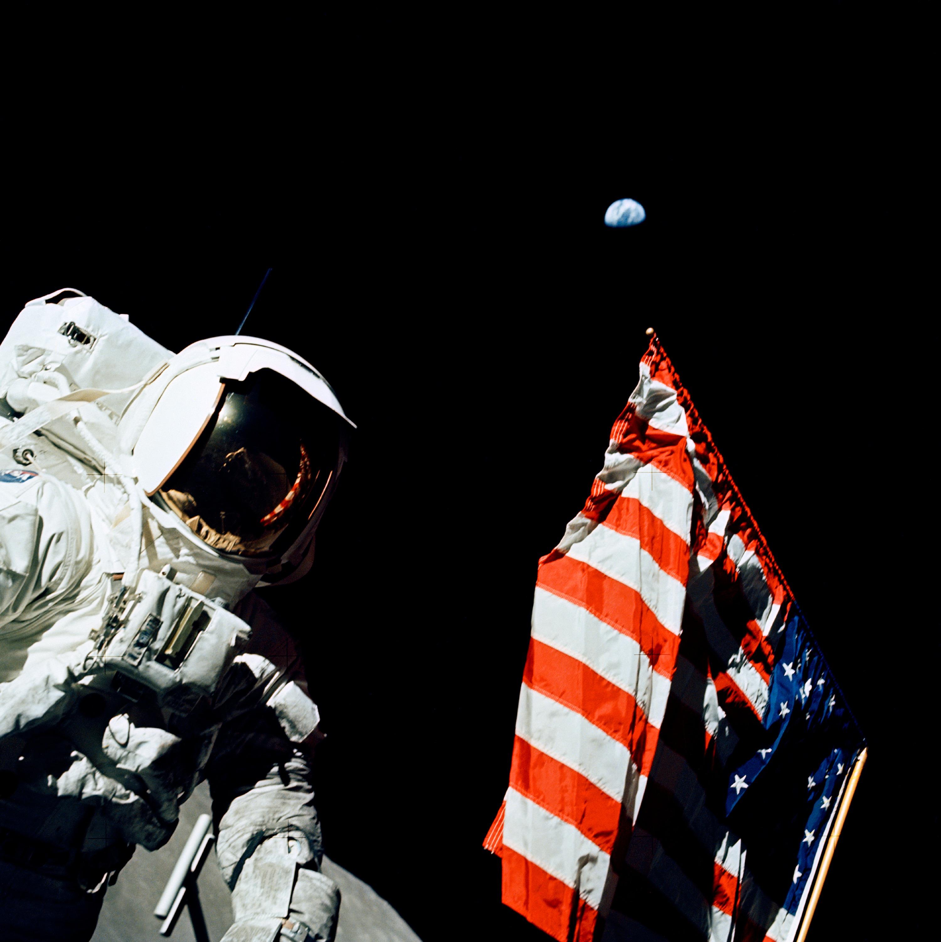Color image of an astronaut and American flag on the Moon with Earth in the background.