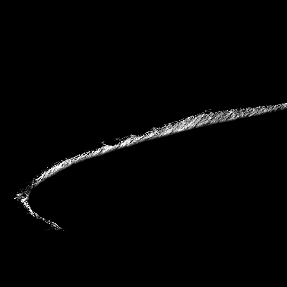 This is an image of Shackleton Crater, an impact crater that lies at the lunar South Pole. The image is engulfed in a sea of darkness, only a sliver of the crater’s rim is illuminated, forming a lit-up half circle. While peaks along the crater's rim are exposed to almost continual sunlight, the interior is perpetually in shadow. This image was captured by Lunar Reconnaissance Orbiter (LRO).