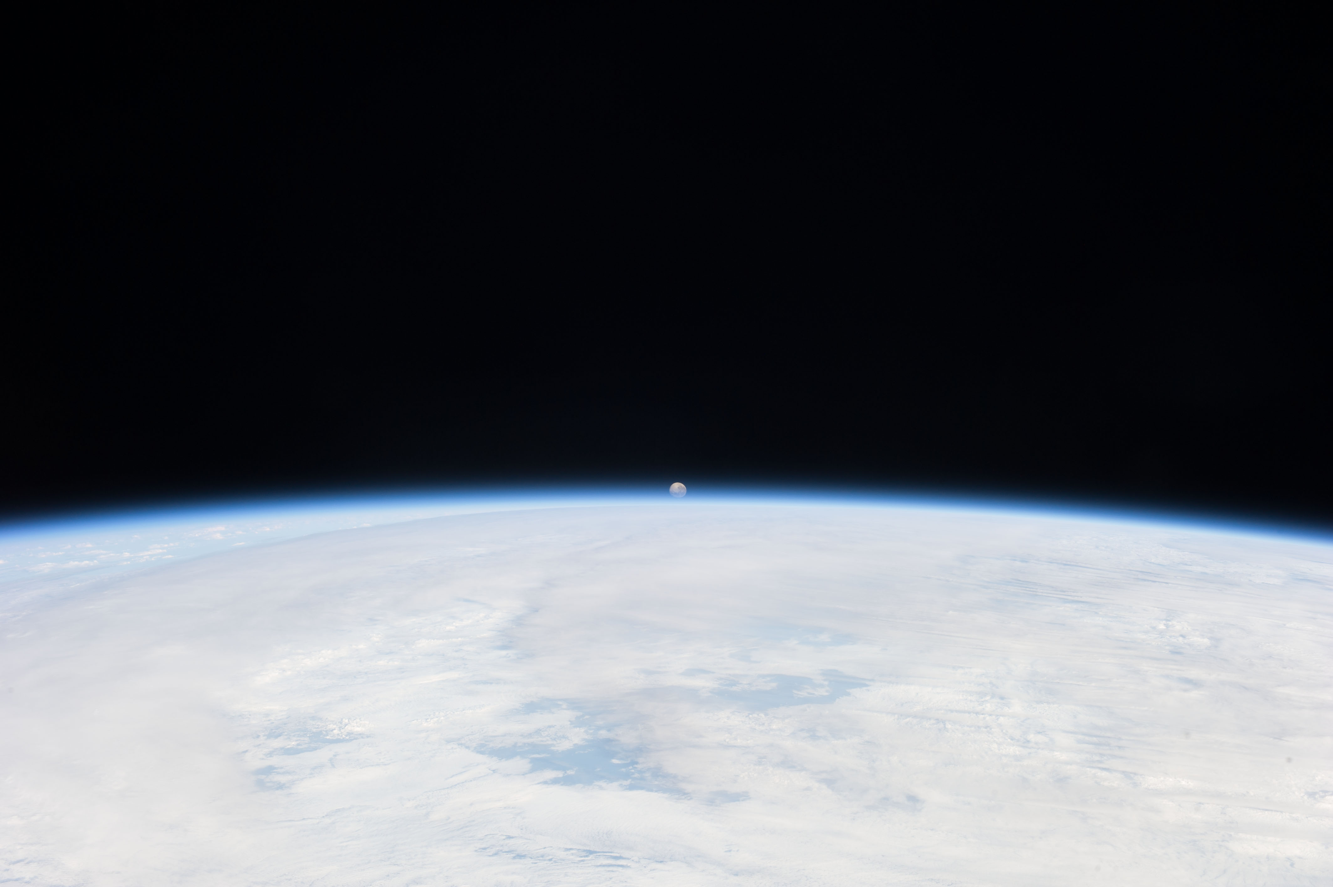 small moon setting in the distance over the curving horizon and the earth's atmosphere 