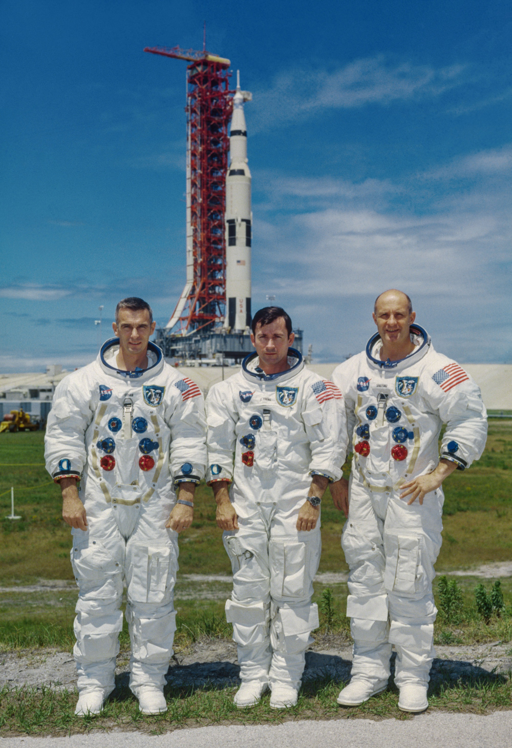 3 astronauts standing in front of rocket