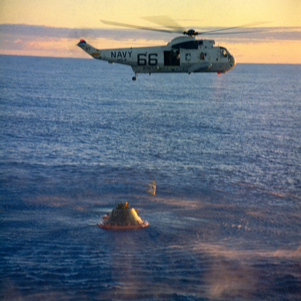 Helicopter lifting astronaut from recovery capsule over Pacific ocean
