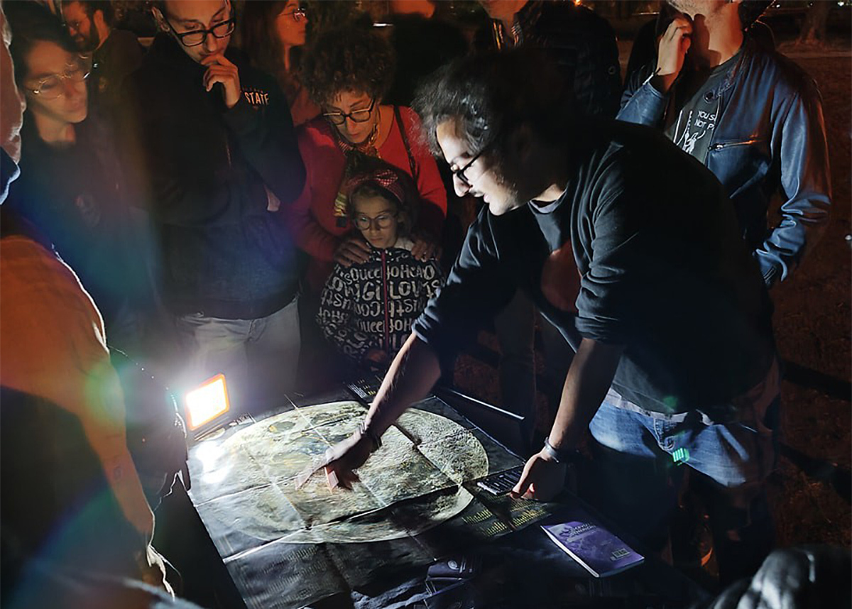 slide 3 - Group of people gather at night around a map of the Moon.