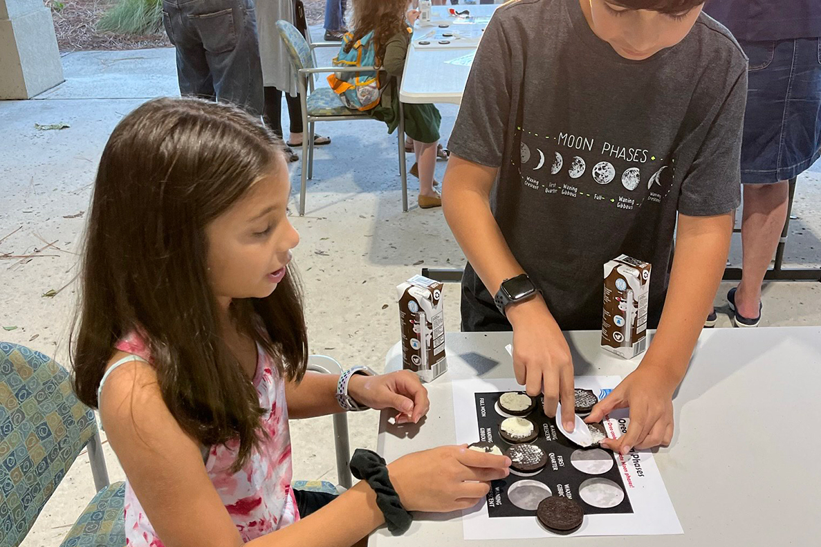 Two young people at a table crafting a project with Oreo cookies to resemble the phases of the Moon.