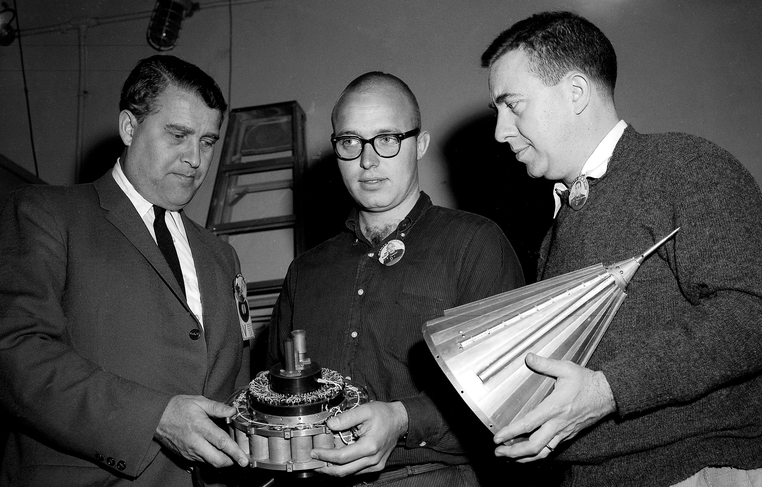 Black and white image of three men holding a small, conical spacecraft.