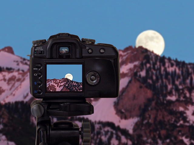 Composite image of a camera in front of a mountain landscape with moon over the horizon