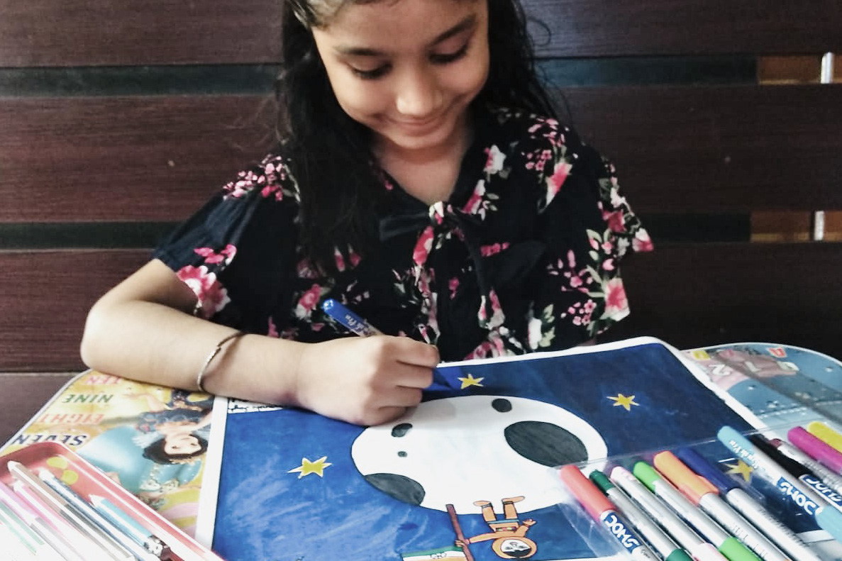 Smiling girl drawing and coloring a picture of the Moon.