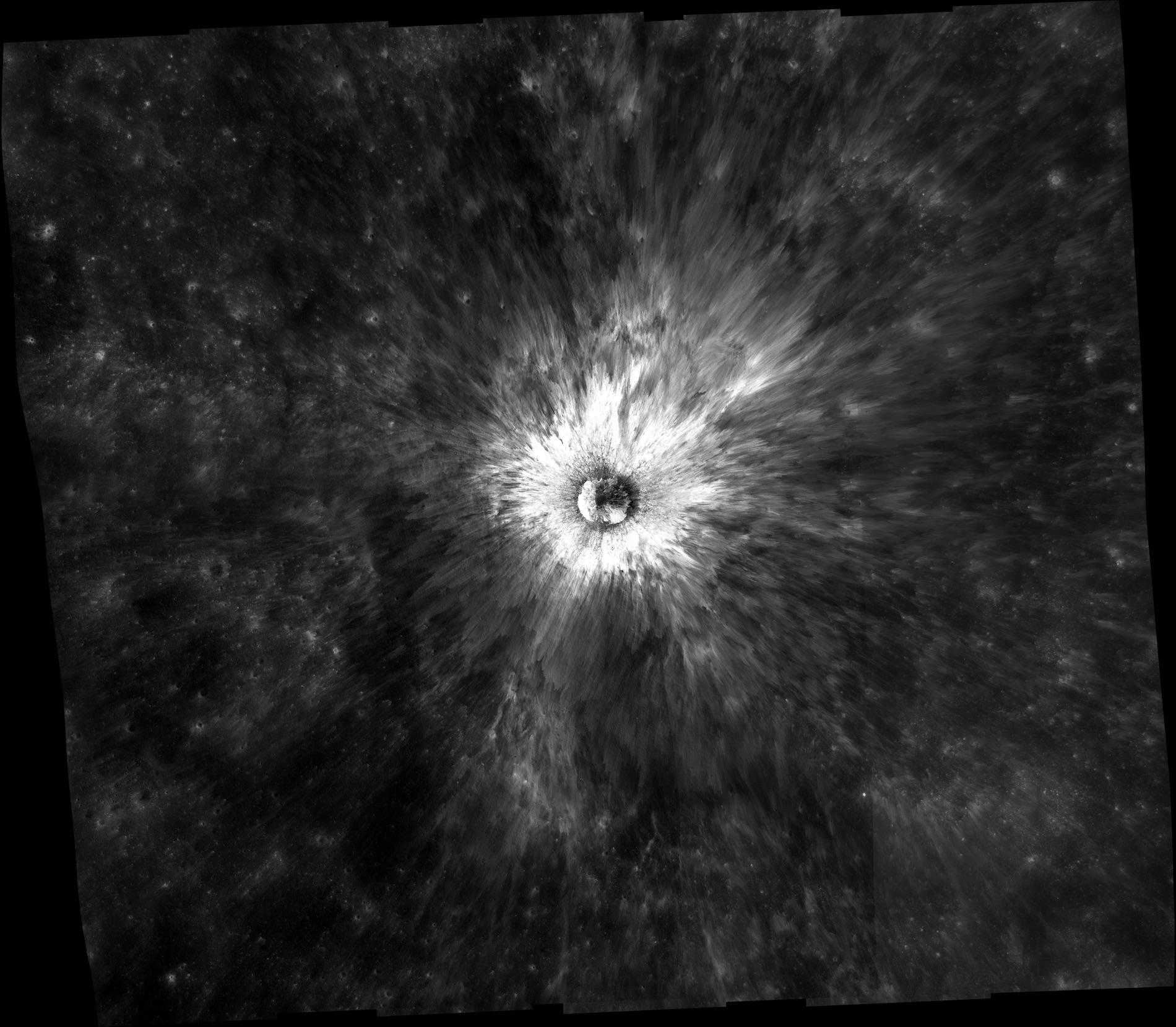 Image of a crater on the Moon. White rays spread out from a circle in the middle over a dark gray background. 